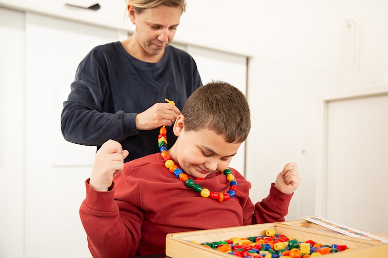 Samen met de leerkracht maakt het kind een kleurrijke kralenketting.