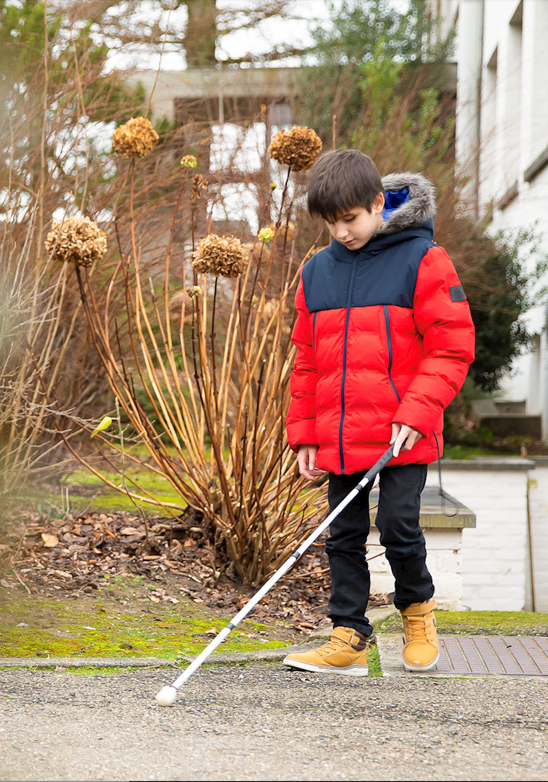 Blinde jongen wandelt met witte stok door het park.