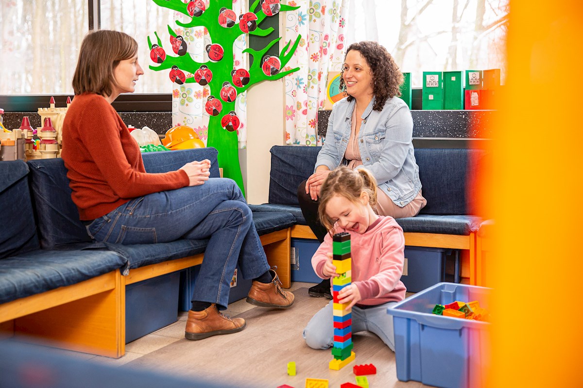 De zorgregisseur bespreekt de mogelijkheden met de ouders, terwijl hun kind aan het spelen is.